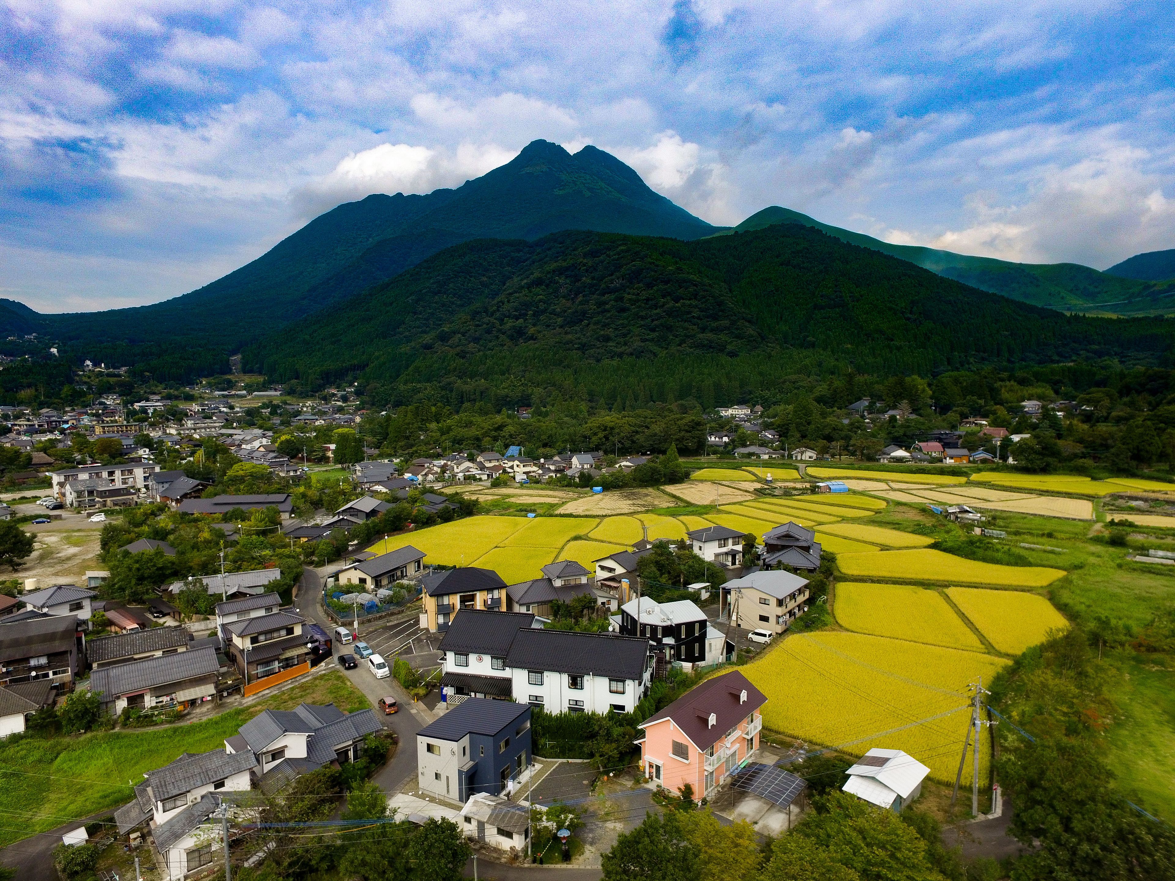 A rural village with houses, fields, and mountains in the background.