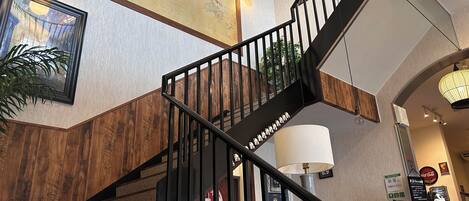 Un interior moderno con una escalera de madera, un mapa del mundo, un cuadro enmarcado y un cartel de Coca-Cola.