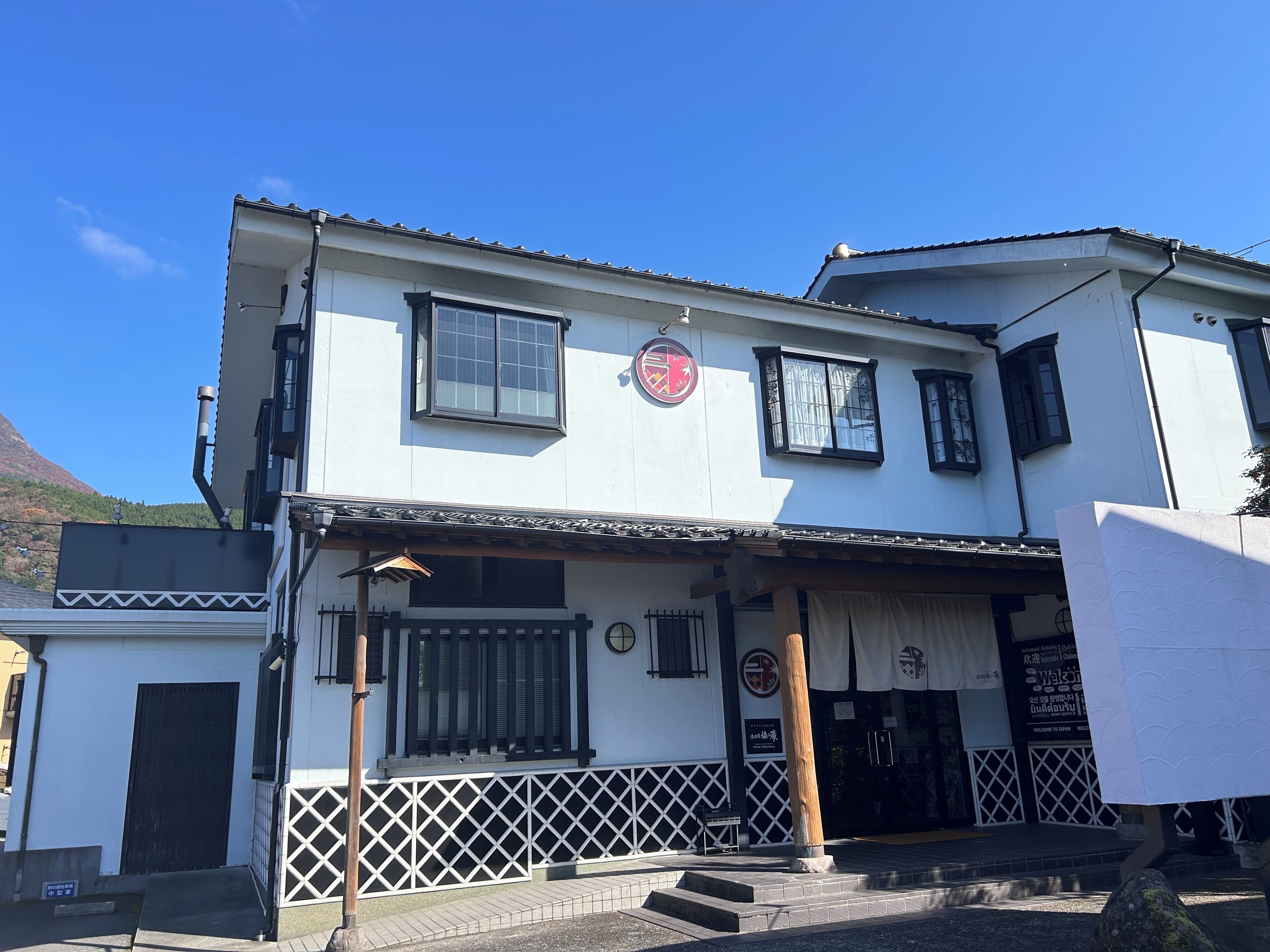 A two-story building with a white facade, a black roof, and a traditional Japanese entrance with a wooden gate.