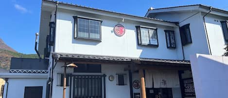 A two-story building with a white facade, a black roof, and a traditional Japanese entrance with a wooden gate.