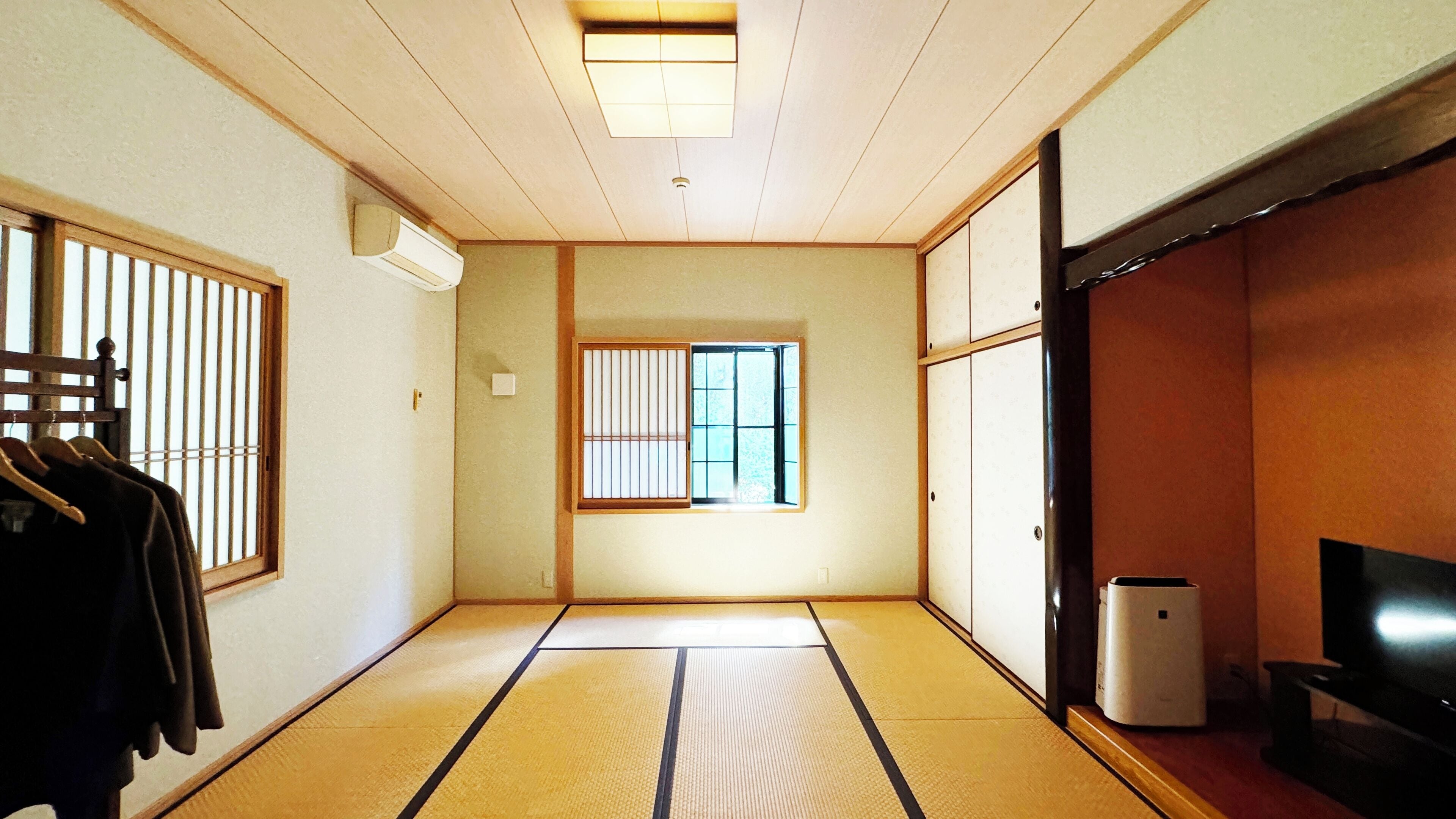 A traditional Japanese room with tatami flooring, a sliding door, a window with shoji screens, and a television.