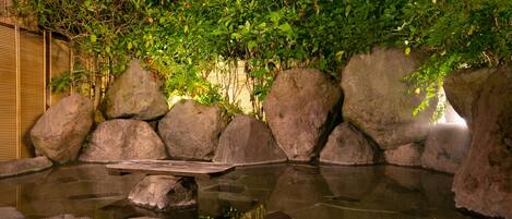 A tranquil garden with a pond, surrounded by large rocks and lush greenery.