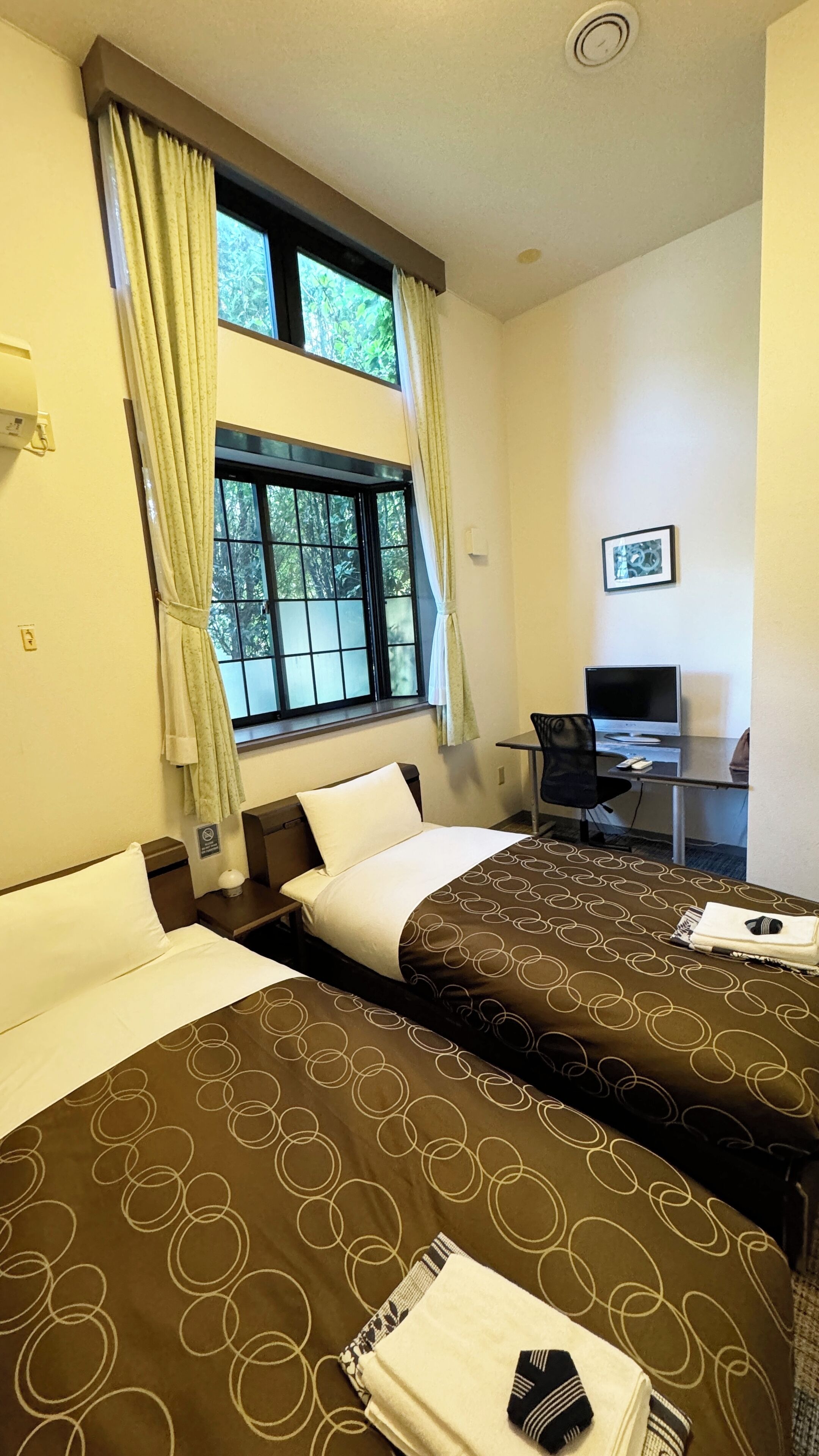 A hotel room with two beds, a desk with a computer, and a window with curtains.