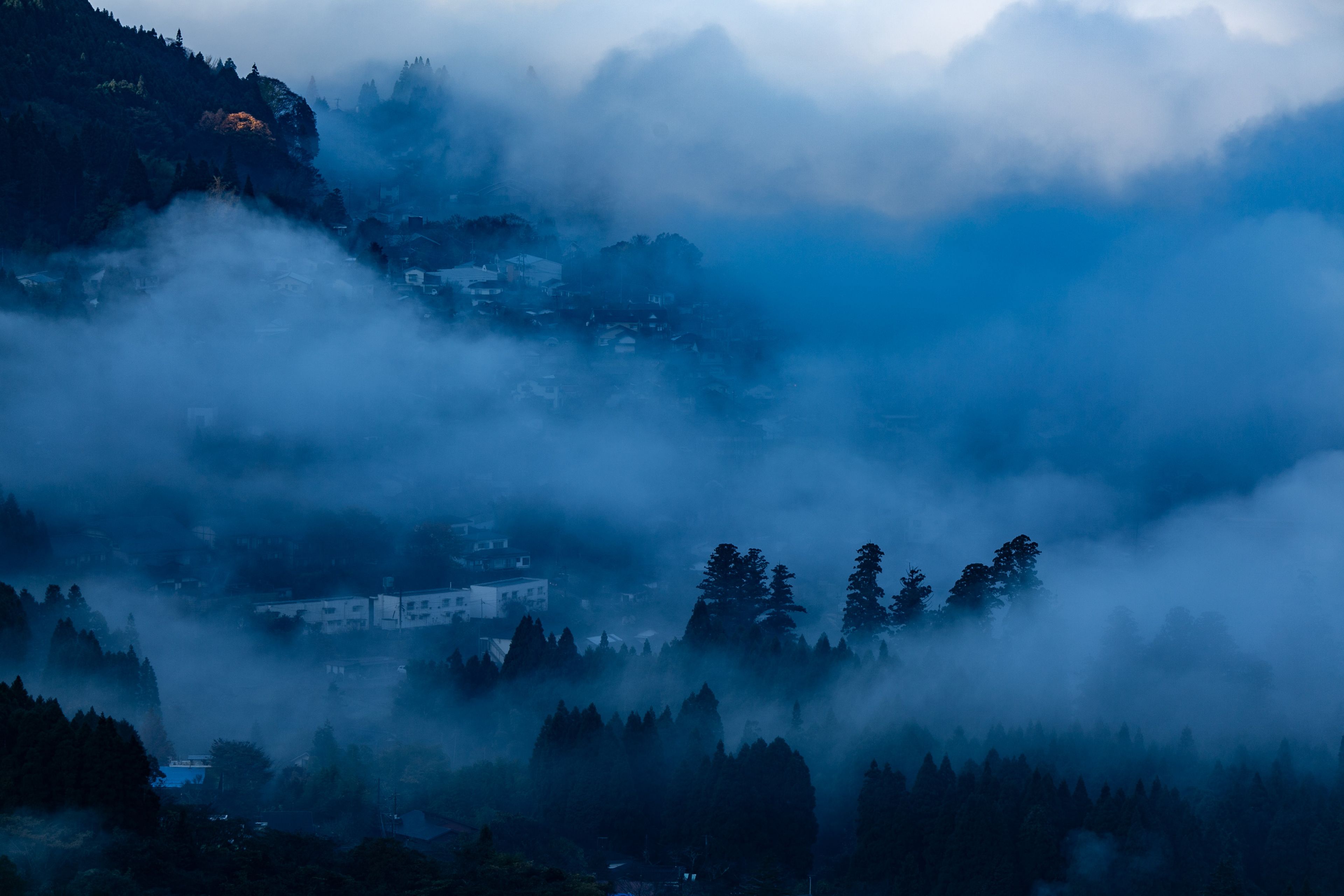 A mountainous landscape with a village nestled among trees and fog.