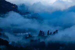 A mountainous landscape with a village nestled among trees and fog.