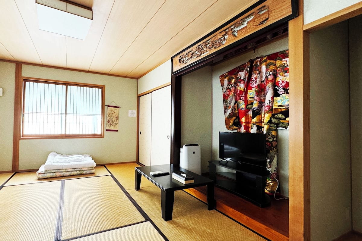 A traditional Japanese room with tatami flooring, a futon bed, a television, and a sliding door with a colorful tapestry.