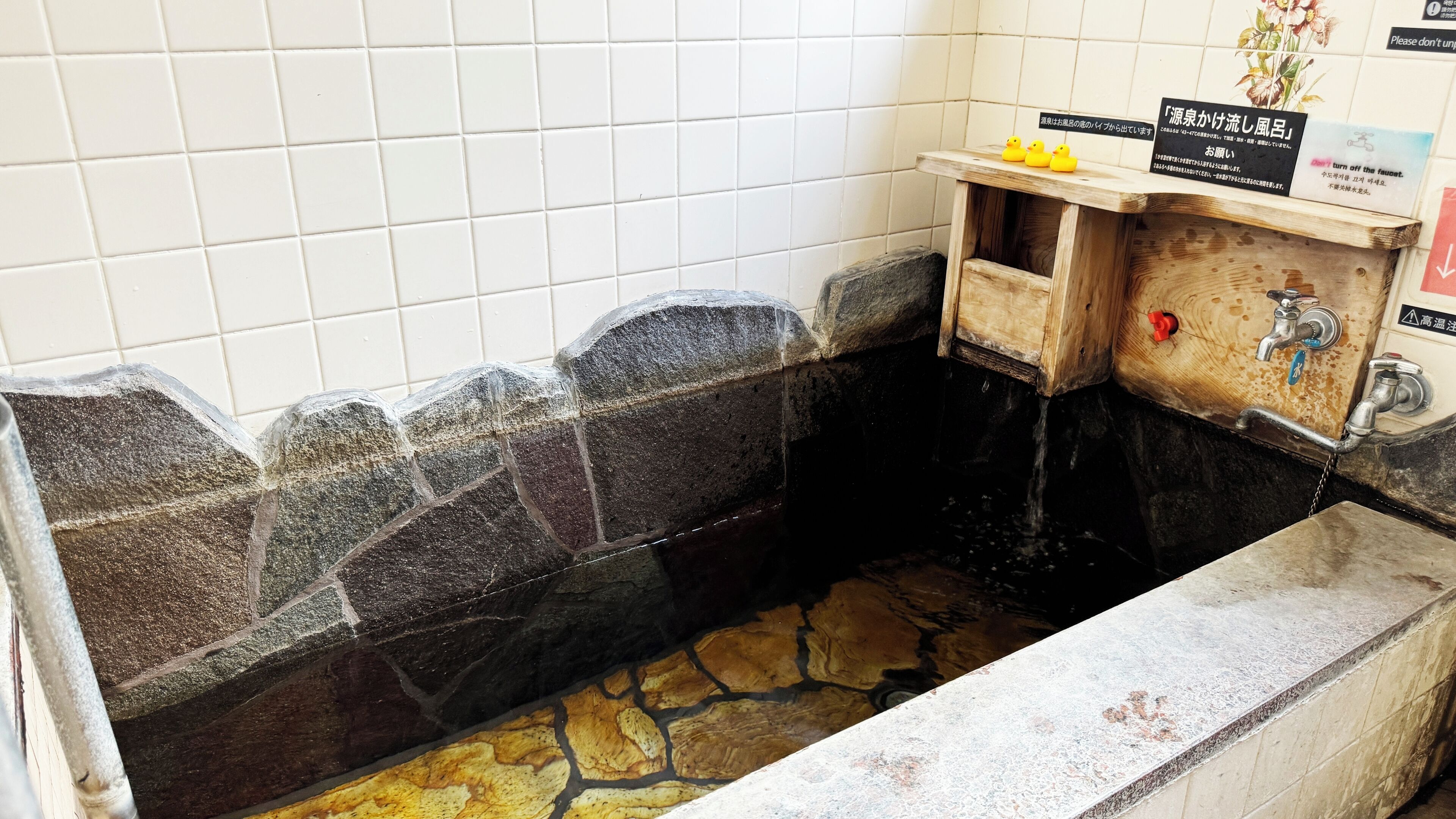 A stone-lined sink area with a wooden shelf holding rubber ducks and a sign.