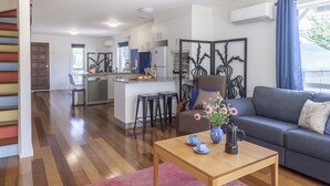 A modern living room with a grey sofa, a wooden coffee table, and a kitchen area in the background. - One of a Kind Apartments (Dickson)
