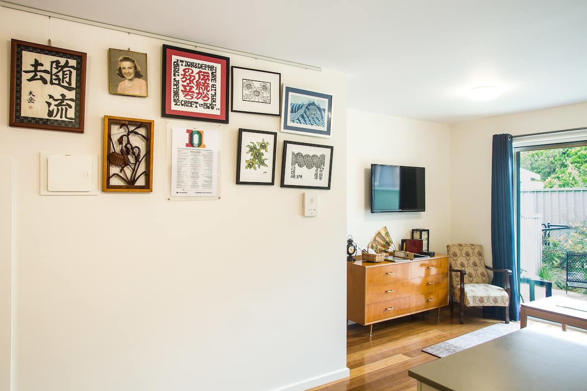 A living room with a wooden floor, a TV mounted on the wall, a wooden cabinet, and a chair.