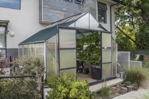 Une serre dotée d’un toit transparent, entourée de plantes et bordée d’un chemin en pierre.