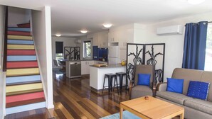 A modern living room with a wooden coffee table, a sofa with blue cushions, and a staircase with multicolored steps. - One of a Kind Apartments (Dickson)