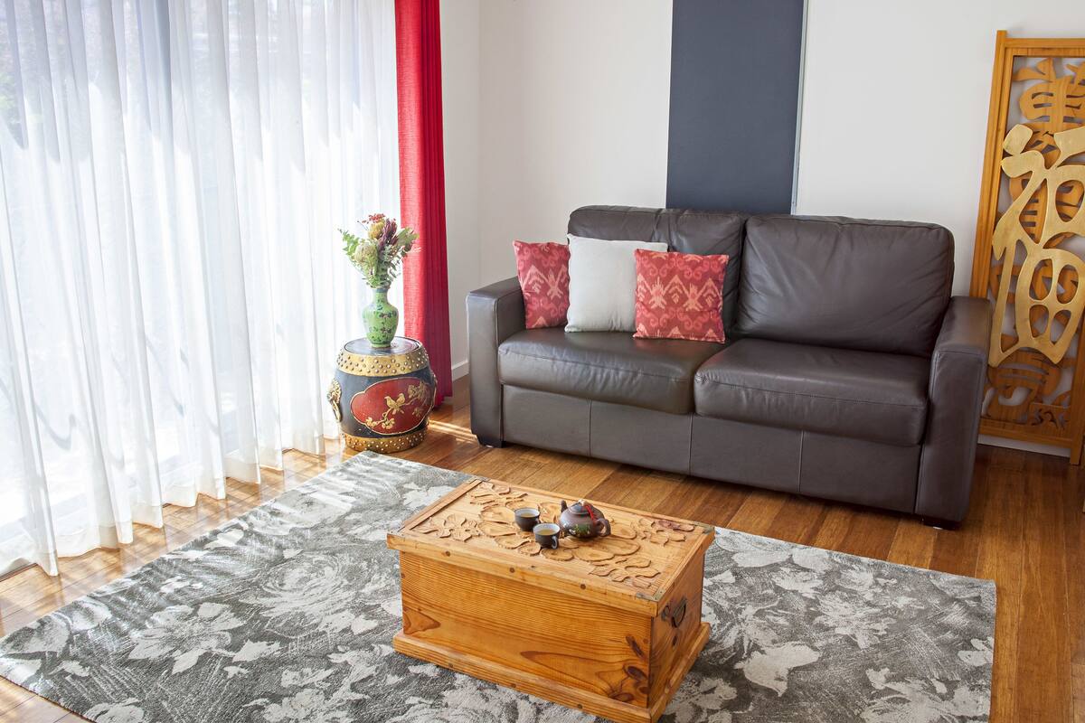 A living room with a sofa, a decorative wooden chest, a vase with flowers, and a traditional wooden screen.