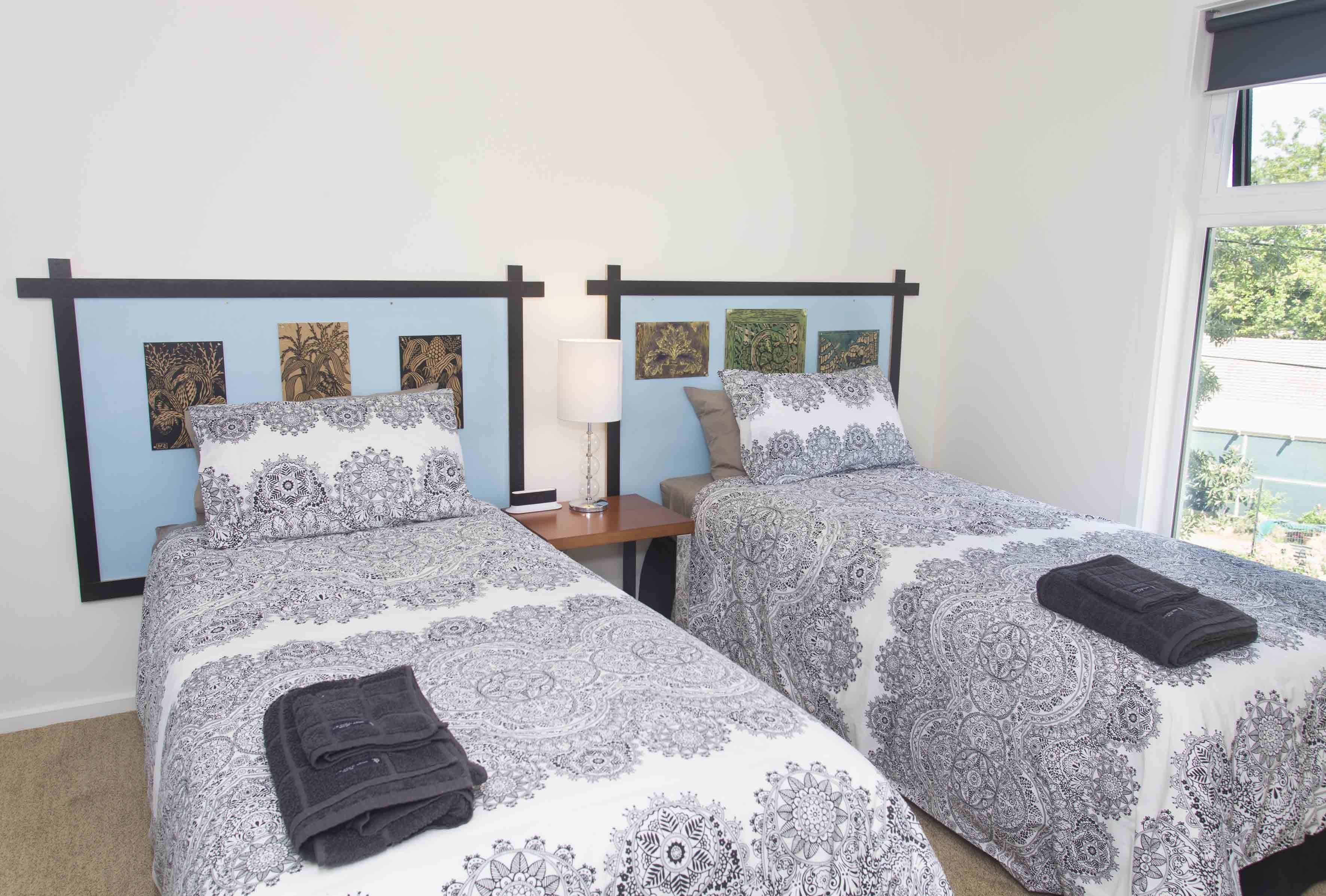 A bedroom with two beds, each with a patterned bedspread and matching headboards. There is a nightstand with a lamp between the beds.