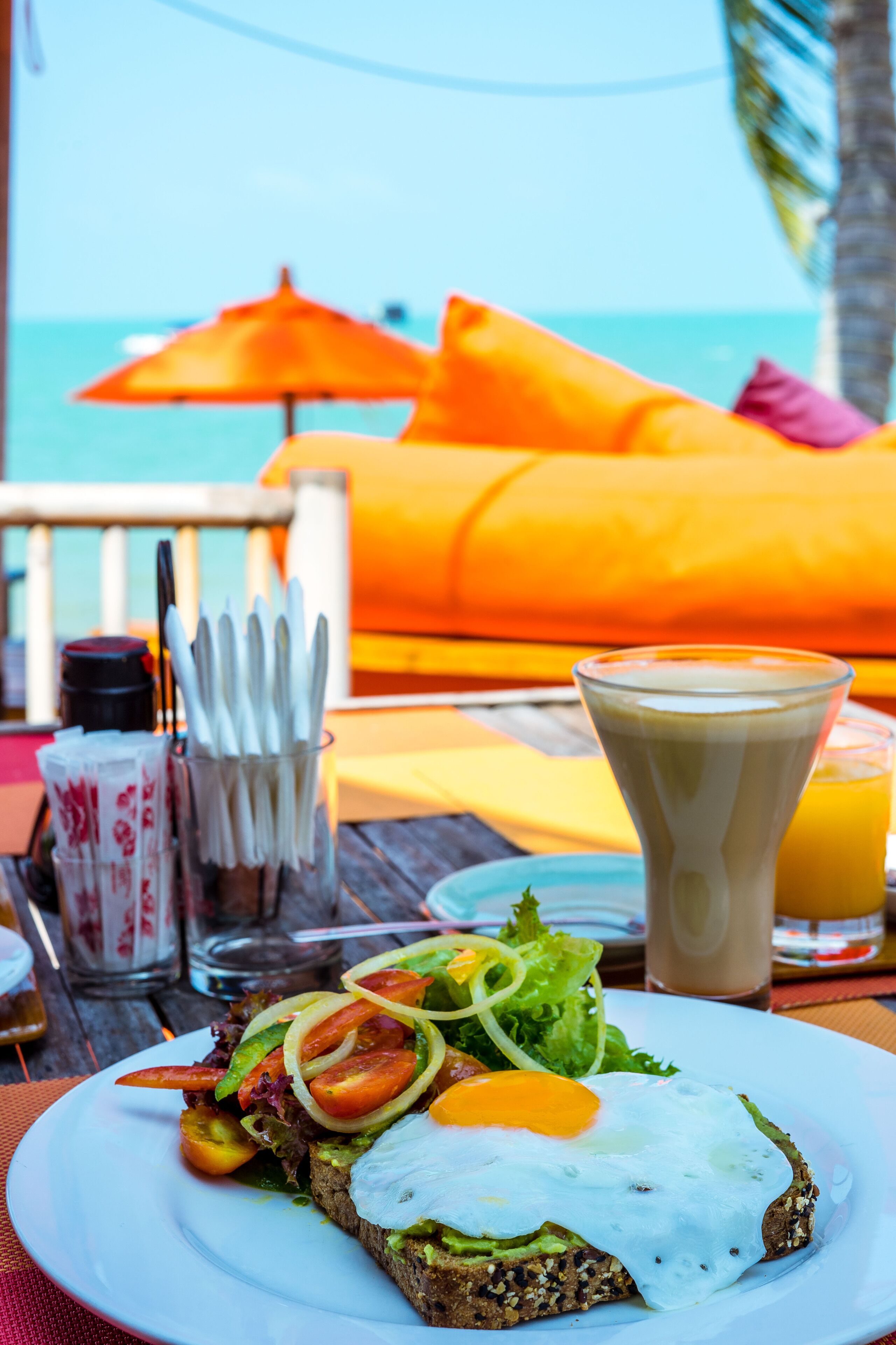 Morgenmad med en tallerken mad, et glas appelsinjuice og en kop kaffe på et bord med en parasol i baggrunden.