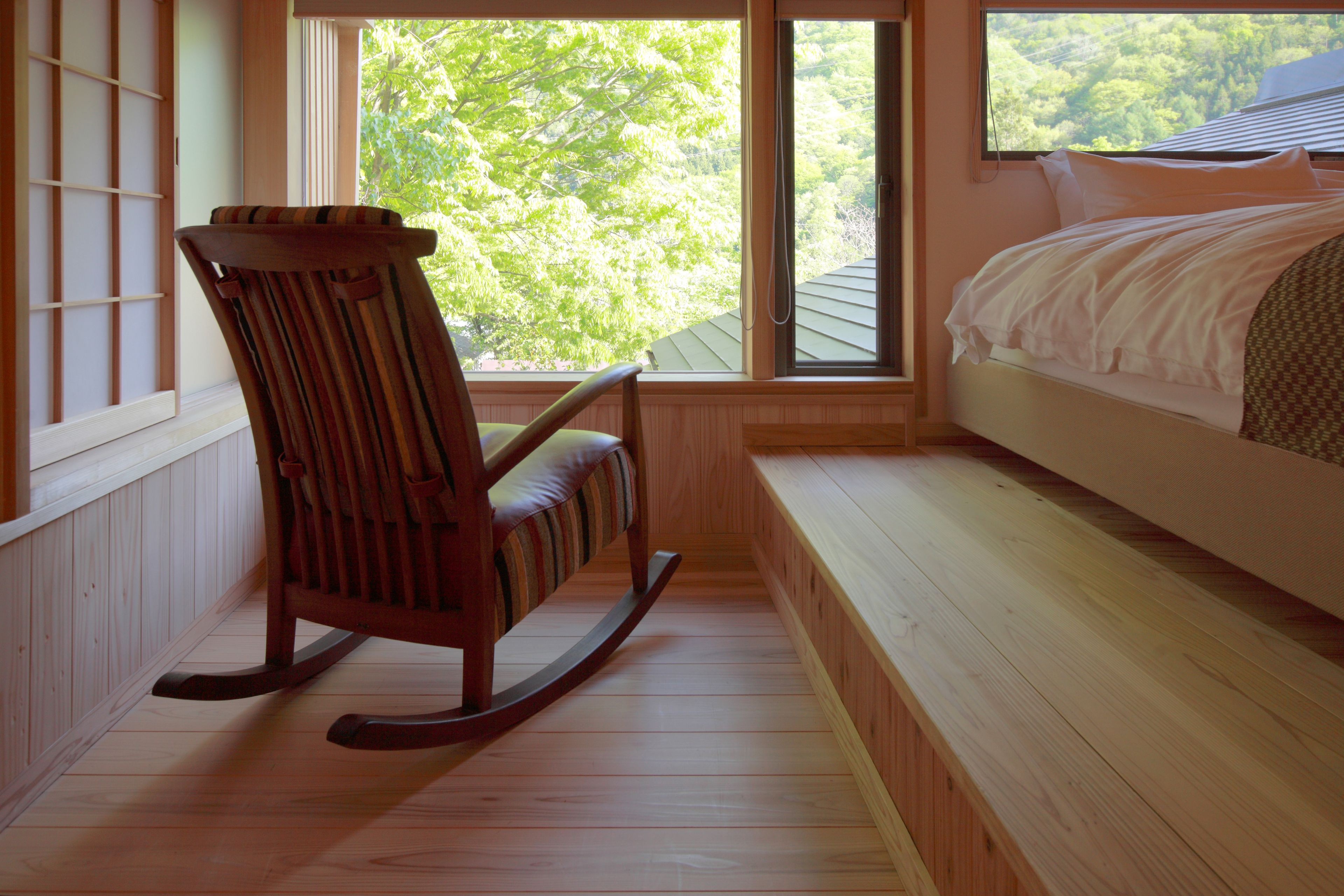 A bedroom with a bed, a rocking chair, and a window with a view of trees.