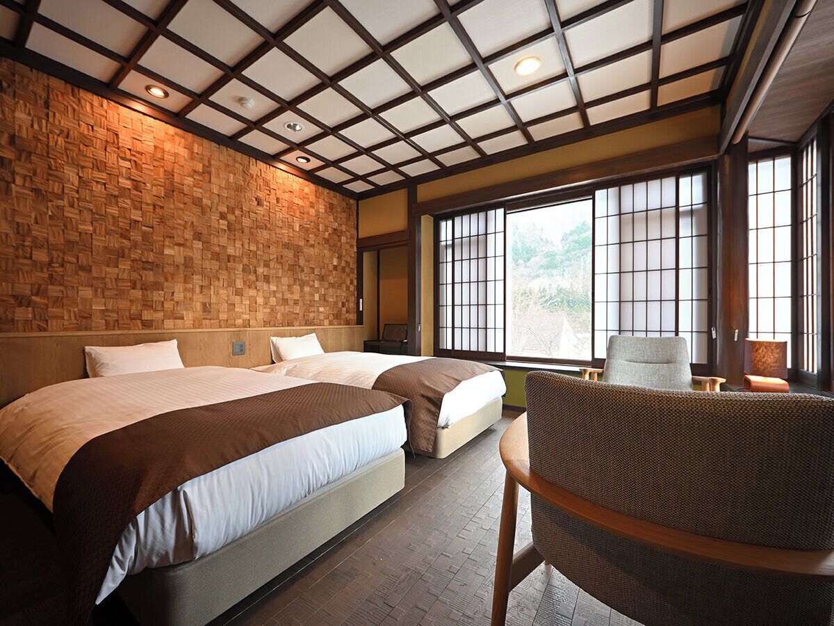 A hotel room with two beds, a large window with a view, and a traditional Japanese-style ceiling.