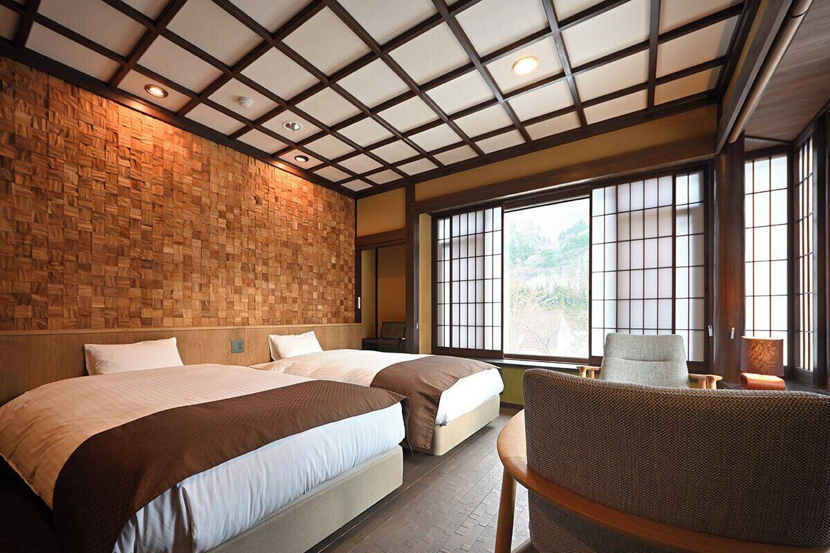 A hotel room with two beds, a large window with a view, and a traditional Japanese-style ceiling.