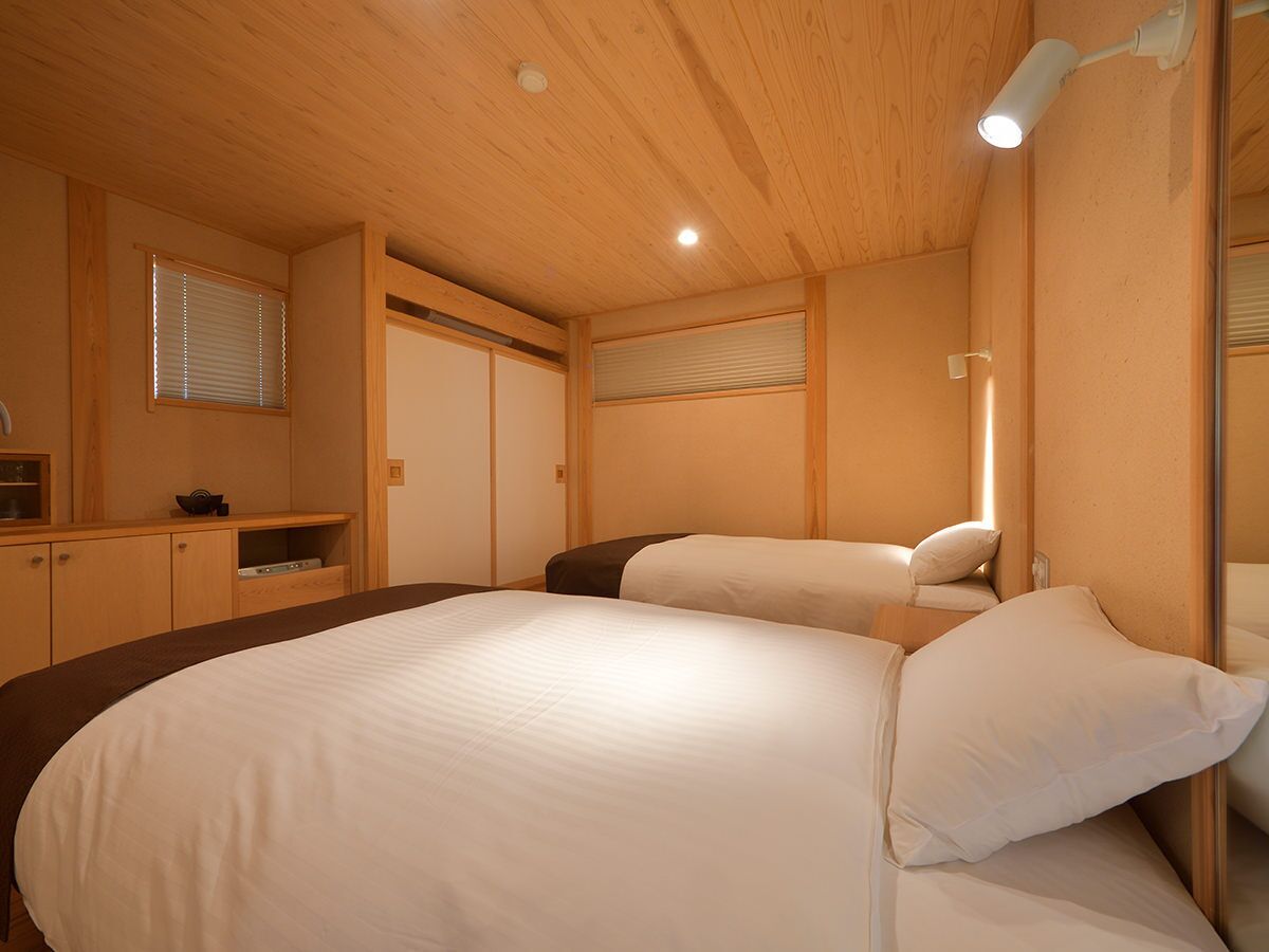A bedroom with a large bed, a bedside table, a mirror, and a window with blinds.