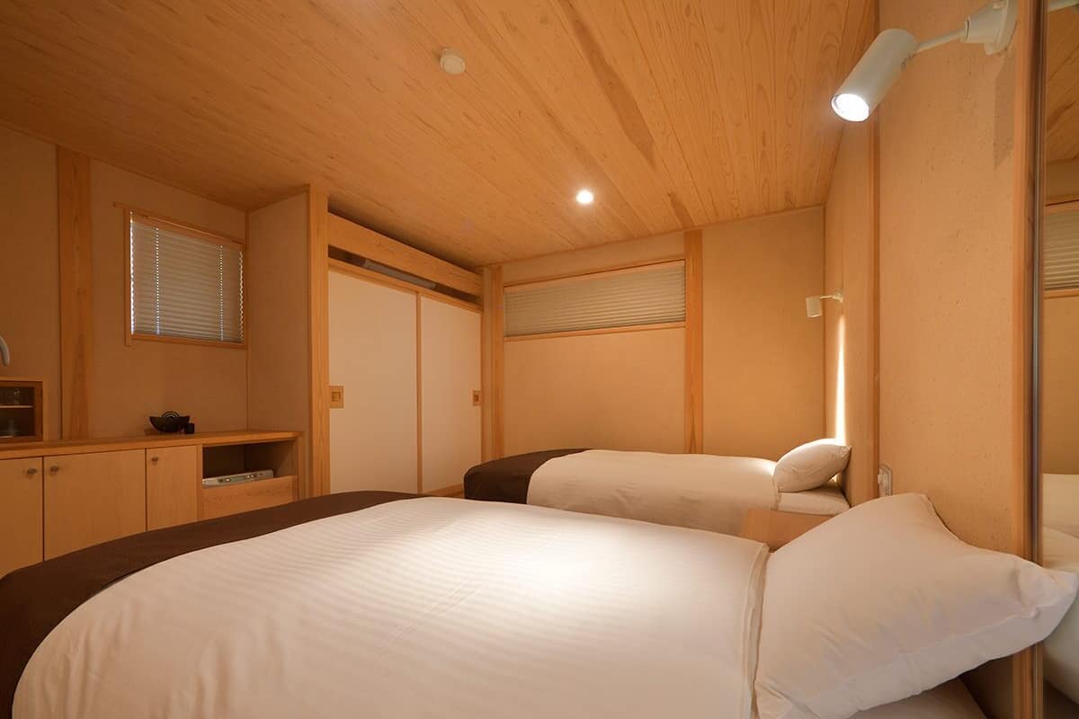 A bedroom with a large bed, a bedside table, a mirror, and a window with blinds.