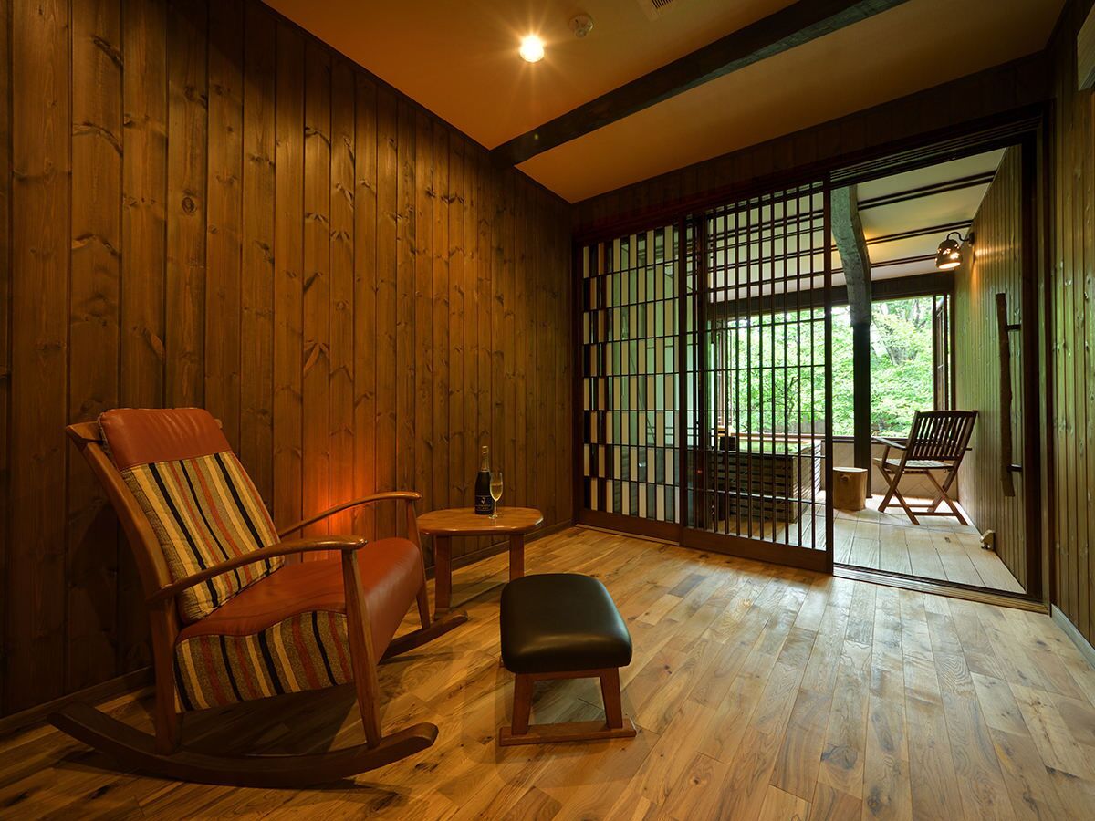 A wooden interior with a rocking chair, a small table with a bottle, and a view through a shoji screen to an outdoor area.