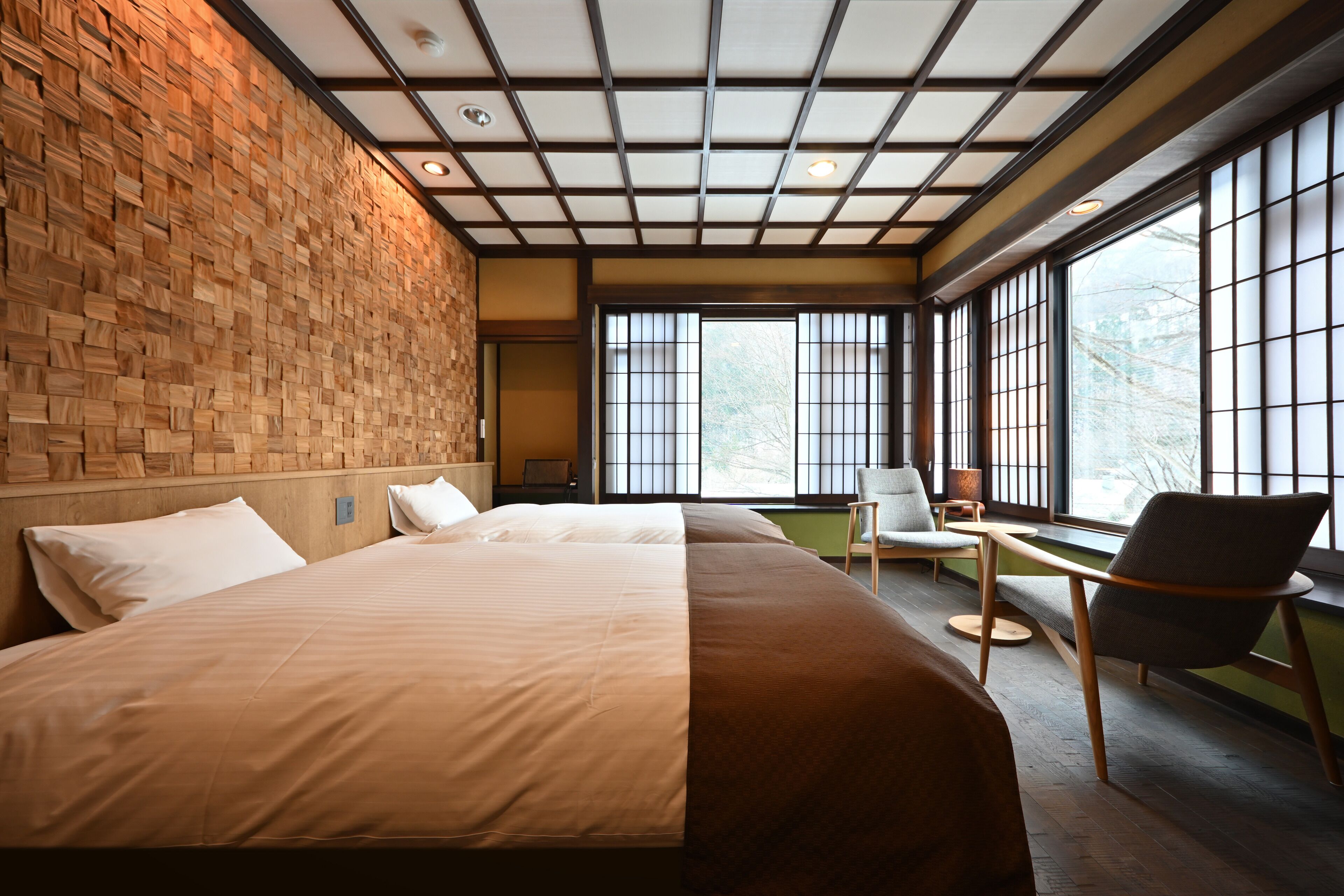 Una habitación de hotel moderna con una cama grande, una zona de estar con sillas y ventanas amplias que ofrecen vistas al exterior.
