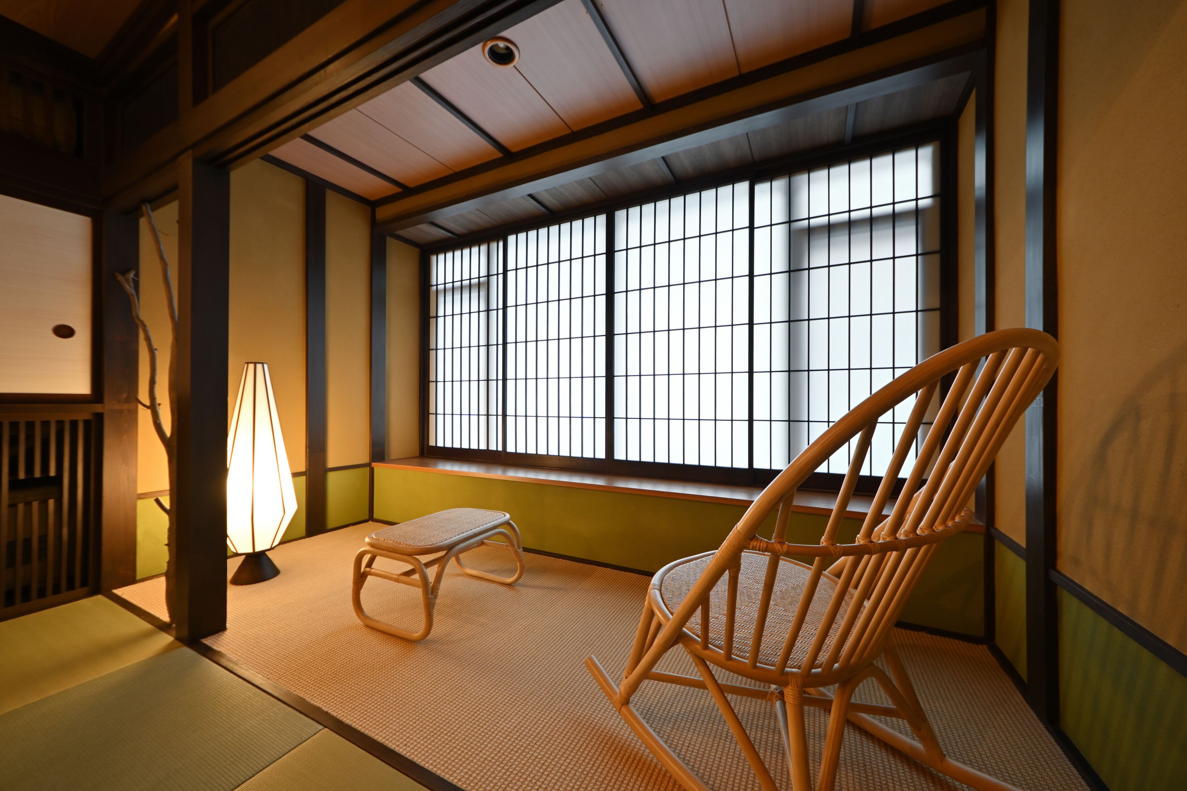 A traditional Japanese room with tatami flooring, a wooden chair, a small table, and a window with a grid pattern.