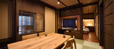 Una habitación tradicional japonesa con una mesa de comedor de madera, sillas, un televisor y una cama.