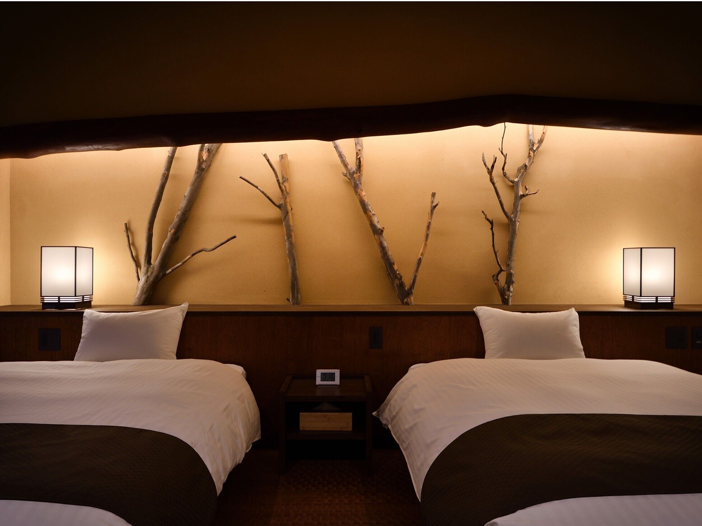 A hotel room with two beds, a wall-mounted clock, and two bedside lamps.