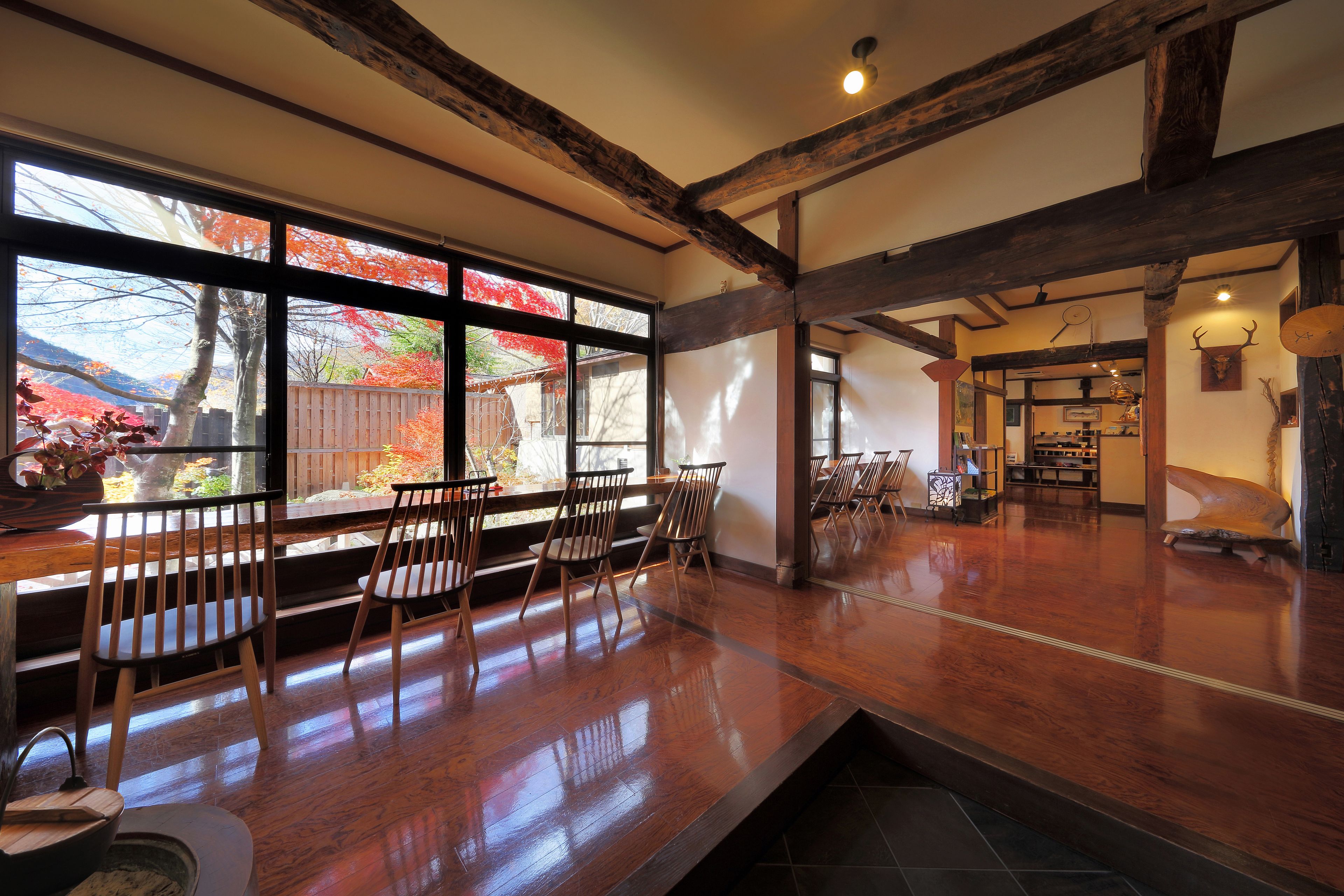 A spacious room with a wooden floor, large windows with a view of autumn trees, and a rustic ceiling with exposed beams.