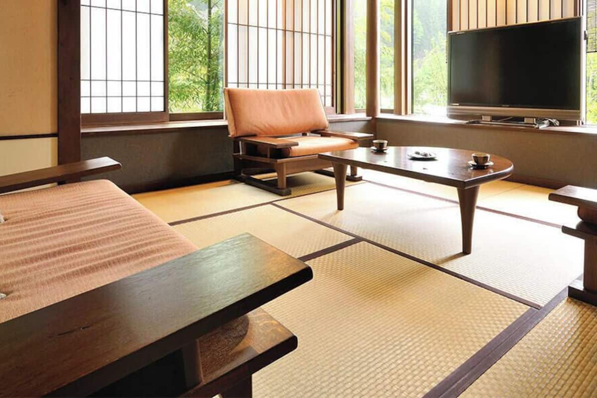 A traditional Japanese room with tatami flooring, a low table, a sofa, and a television.