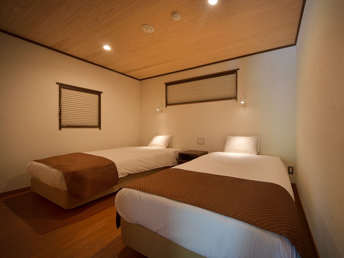 A room with two beds, wooden flooring, and a sloped ceiling with recessed lighting.
