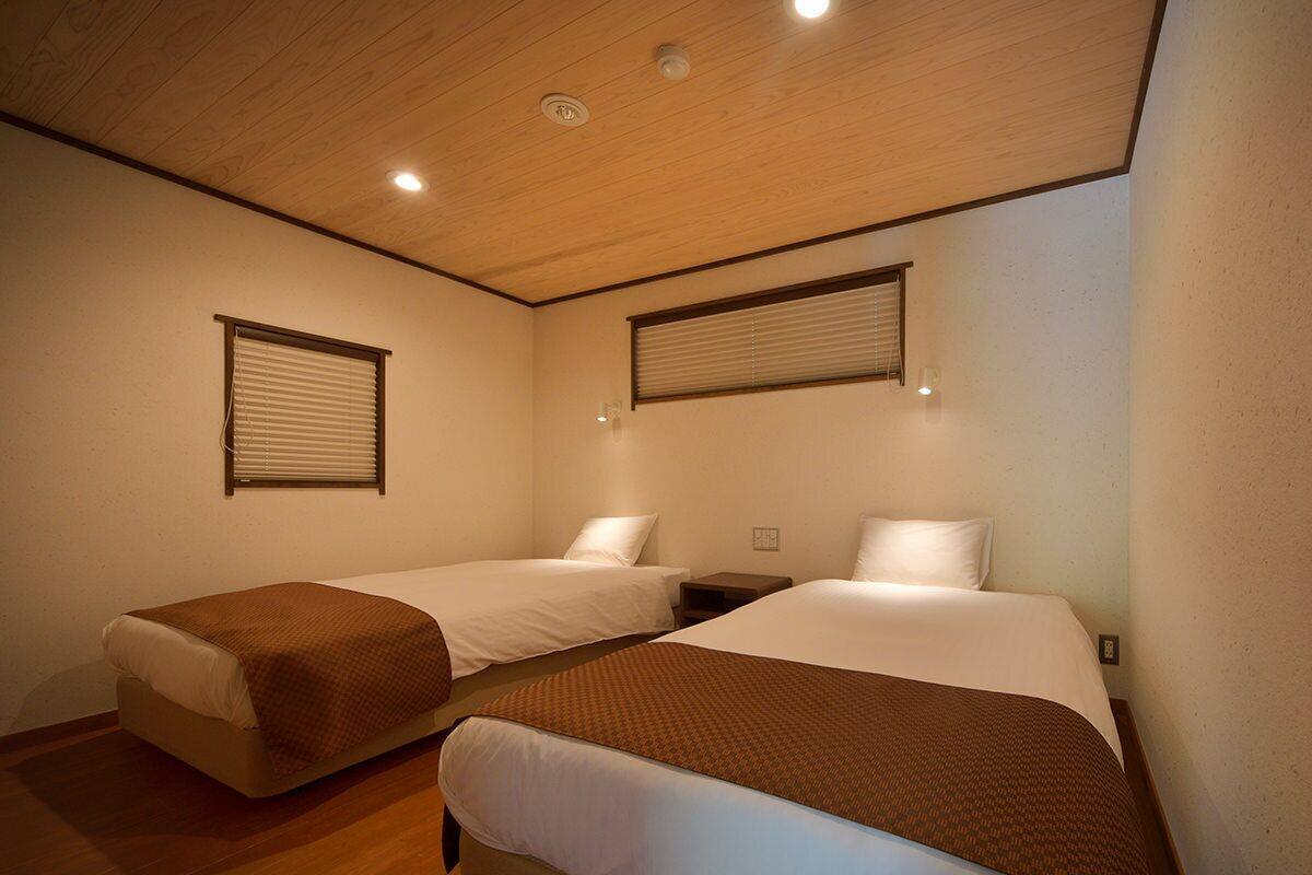 A room with two beds, wooden flooring, and a sloped ceiling with recessed lighting.