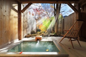 Un espace de détente en bois comprenant un bain à remous, une terrasse en bois et une vue sur un jardin aux couleurs automnales.