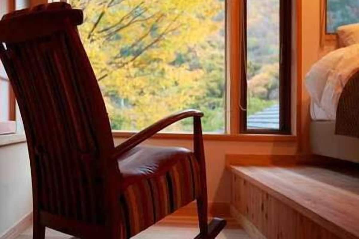 A rocking chair near a window with a view of autumn trees.