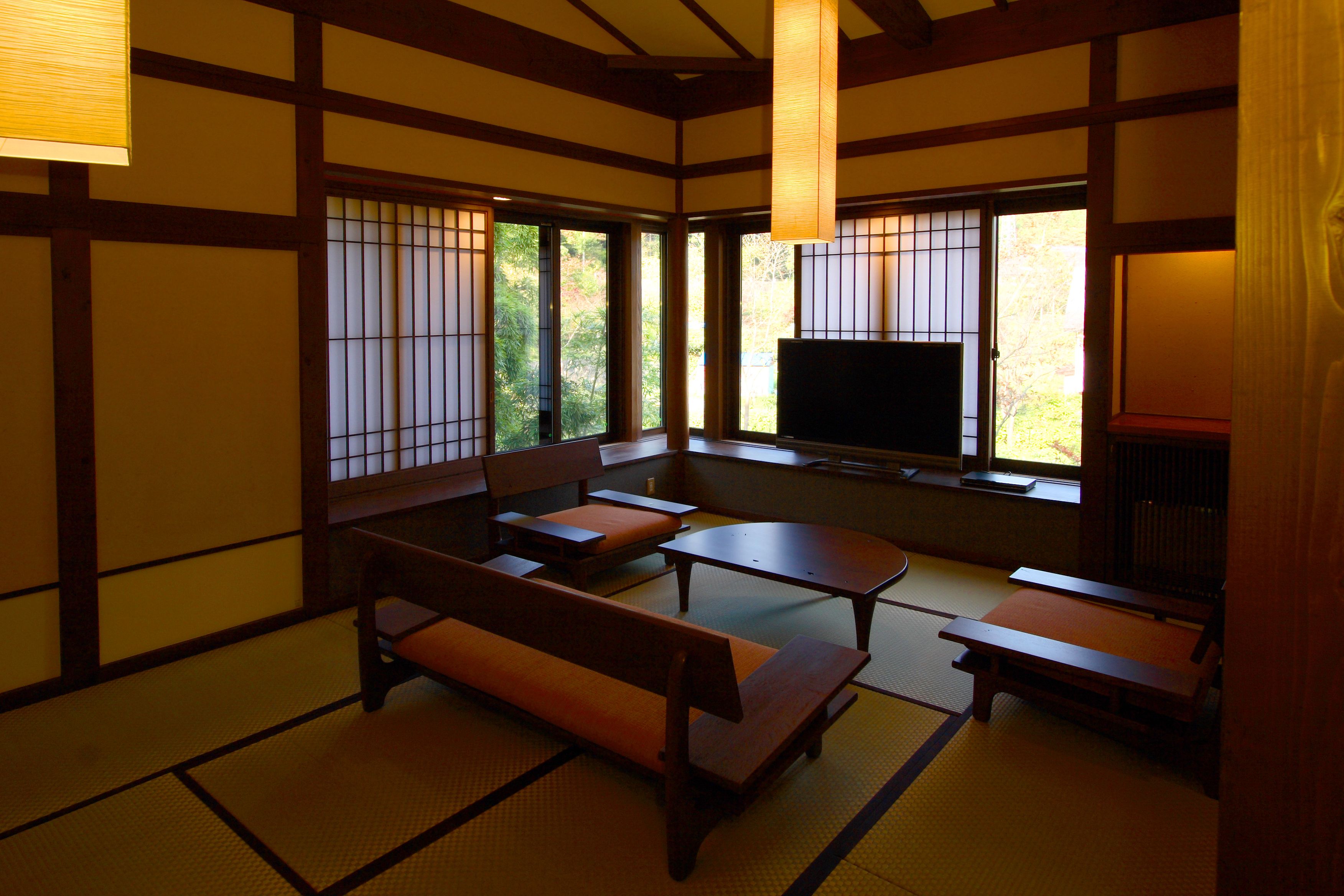 Una habitación japonesa tradicional con suelo de tatami, una mesa baja, bancos y un televisor.