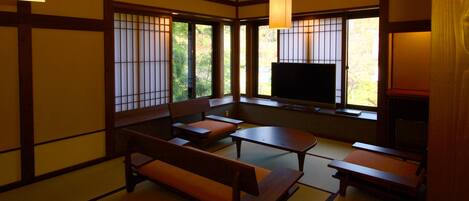 Una habitación japonesa tradicional con suelo de tatami, una mesa baja, bancos y un televisor.
