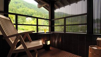 A wooden deck with a view of a forested hillside, a wooden chair, and a small table with a glass.
