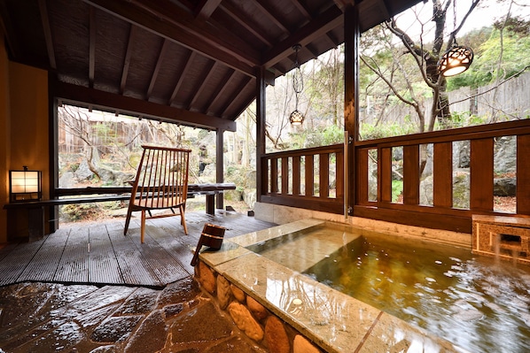 A hot spring area with a wooden deck, stone walls, and a view of a forested area. - Syoubun (Minakami)