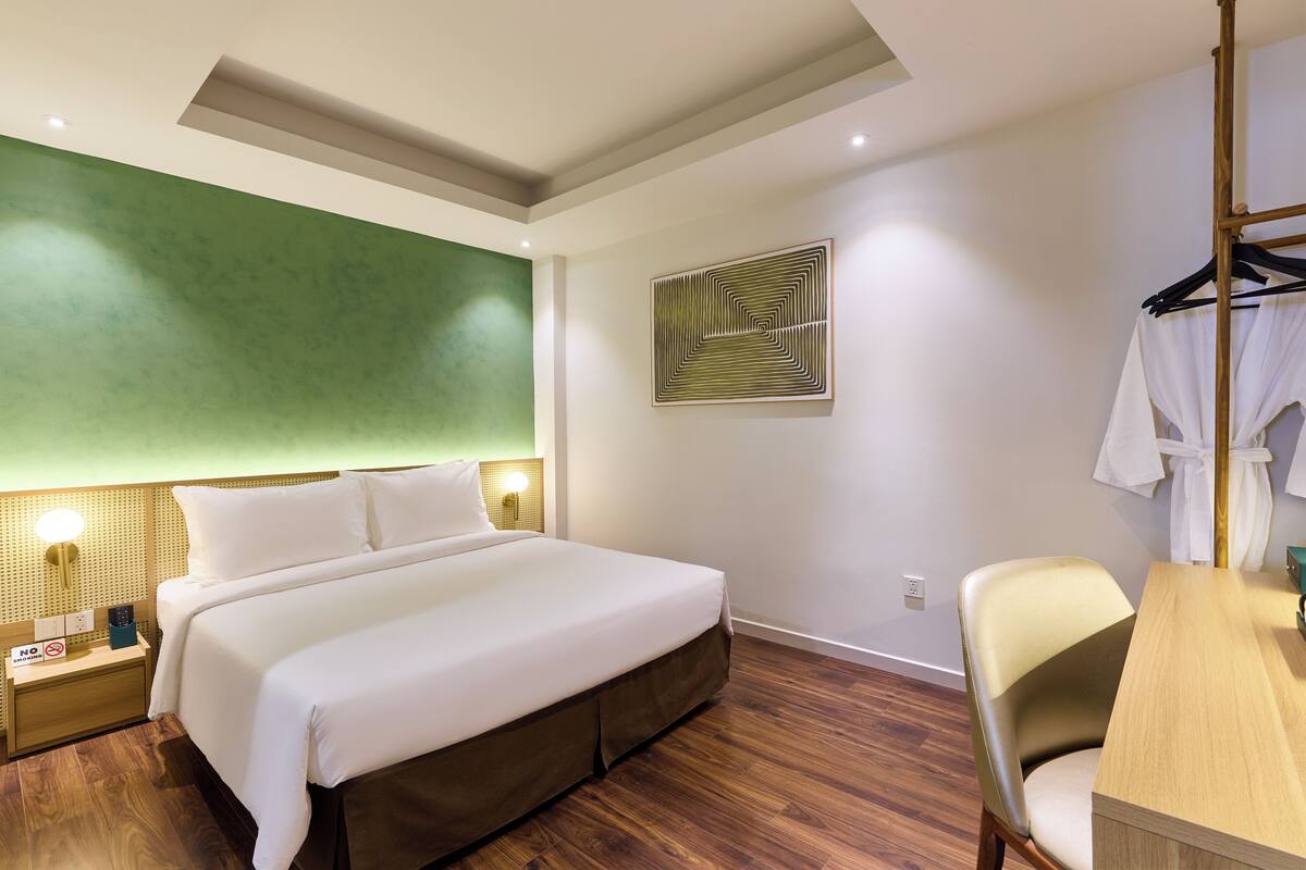 Une chambre d’hôtel avec un grand lit, une table de chevet en bois, un bureau avec une chaise et un mur d’accent vert.