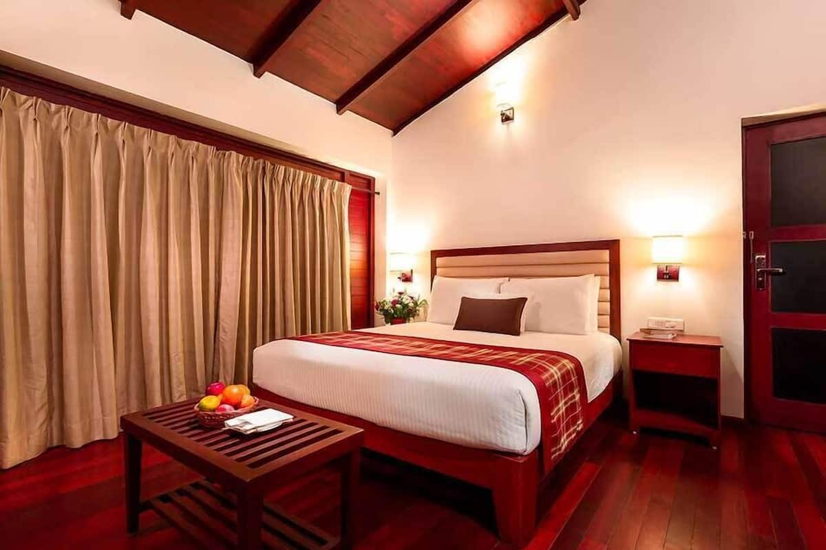 A hotel room with a large bed, wooden headboard, two bedside tables, a small table with fruit, and a red door.