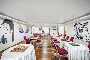 Un salón de conferencias con un tablero de ajedrez, sillas rojas y una mesa blanca.