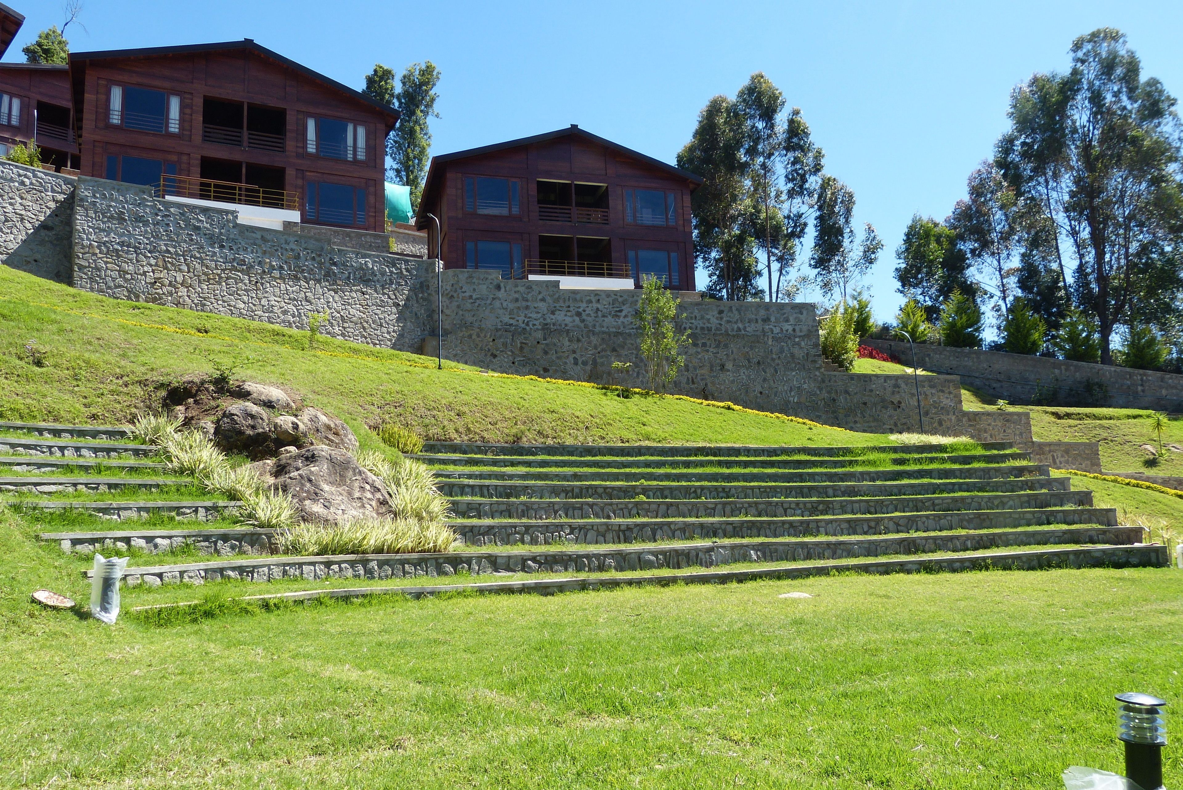 A multi-story building with a stone retaining wall and a grassy slope leading up to it.