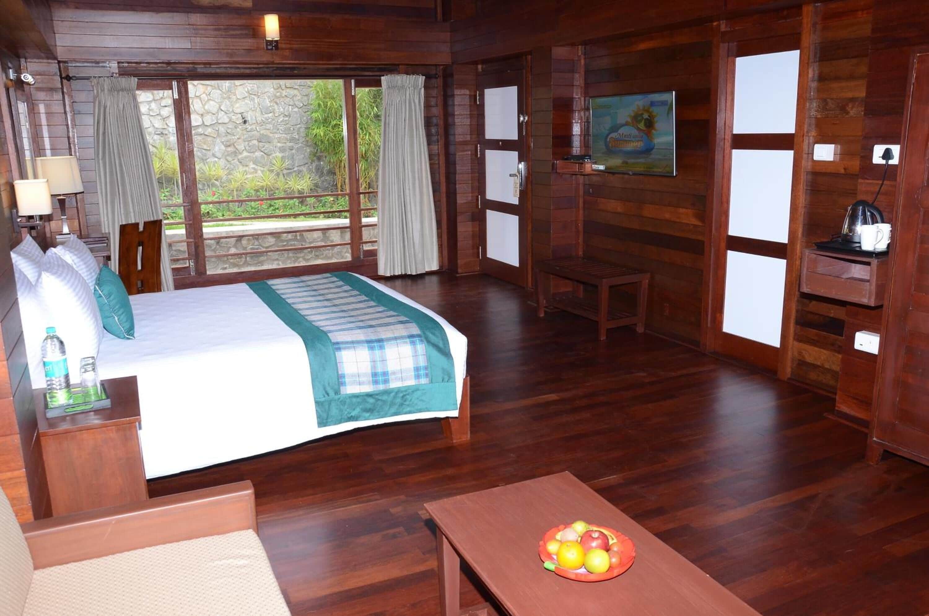A wooden room with a bed, a table with fruit, a TV, and a painting on the wall.