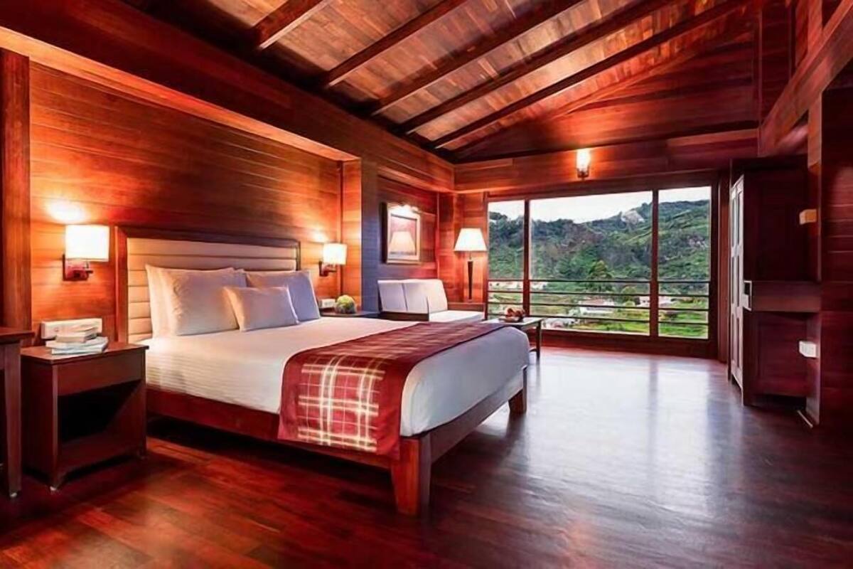 A wooden-floored bedroom with a large bed, nightstands, and a view of a mountainous landscape.
