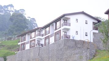 Un edificio de varios pisos con balcones, ubicado en una ladera con un muro de contención de piedra.