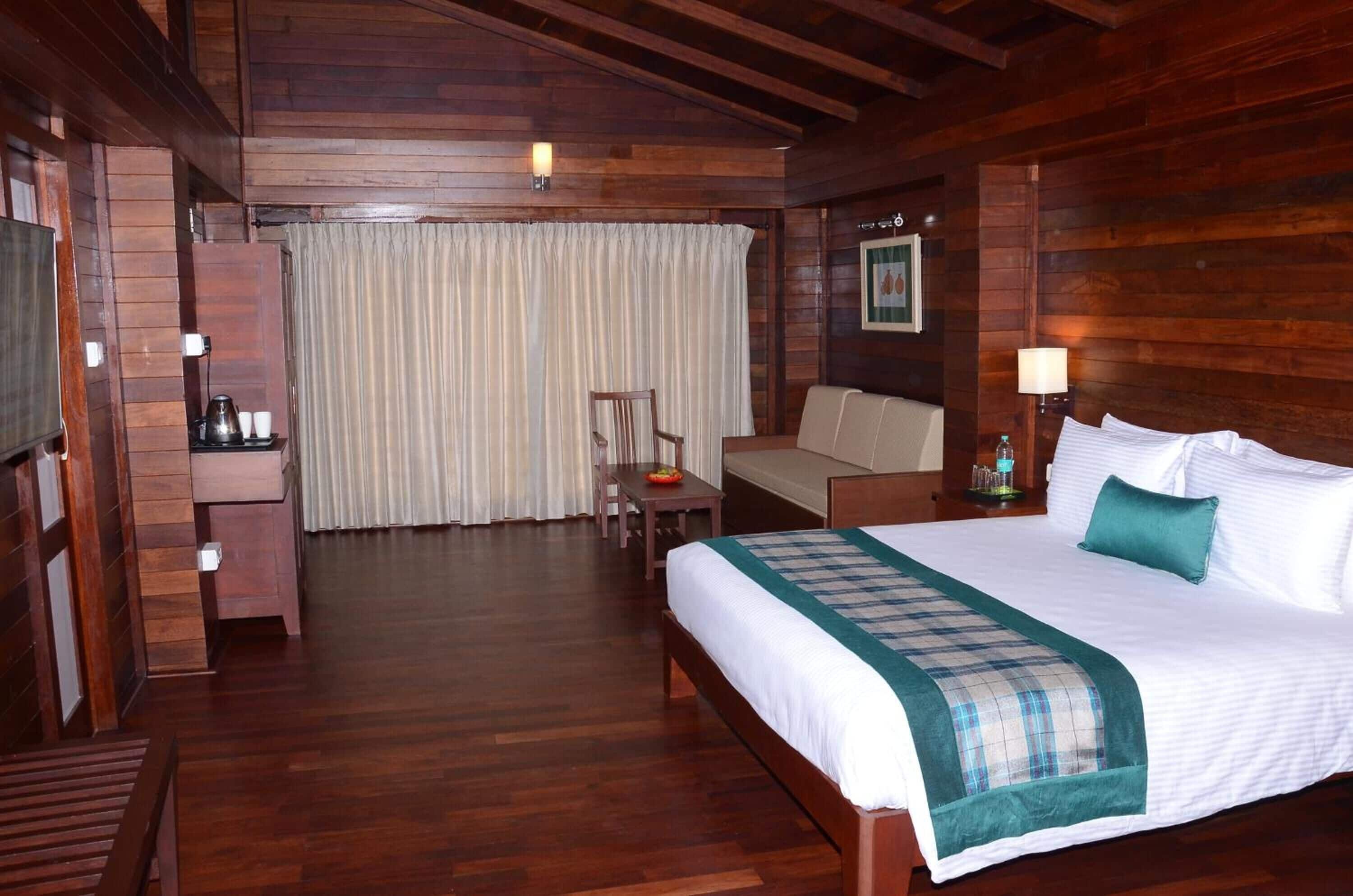 A wooden-floored hotel room with a bed, a small table, a chair, a sofa, and a television.