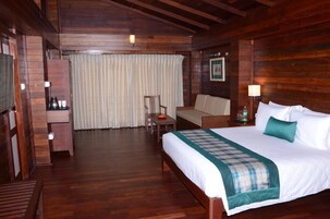 Een hotelkamer met houten vloer, een bed, een klein tafeltje, een stoel, een bank en een televisie.