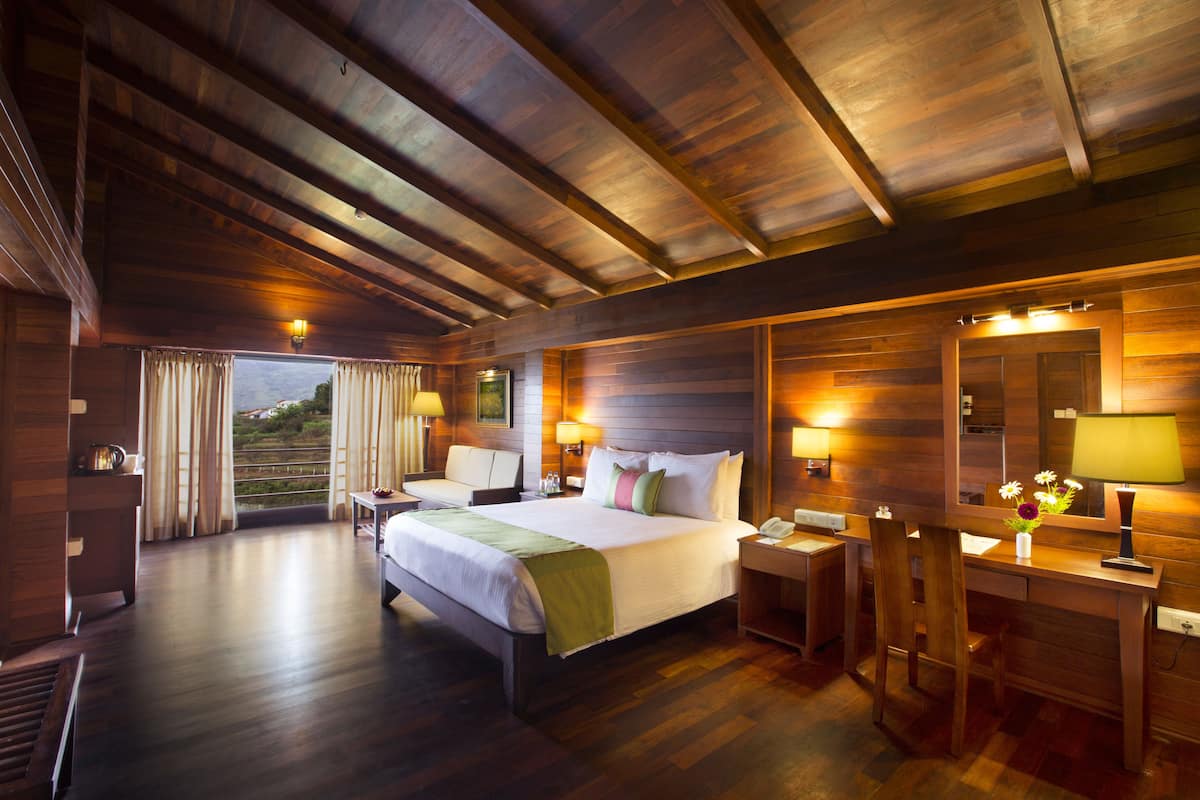 A spacious hotel room with a large bed, a desk, and a chair. There is a view of the outdoors through the window.