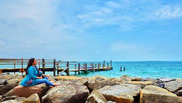 A woman sitting on rocks by a pier with a clear view of the ocean.