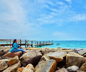 A woman sitting on rocks by a pier with a clear view of the ocean.